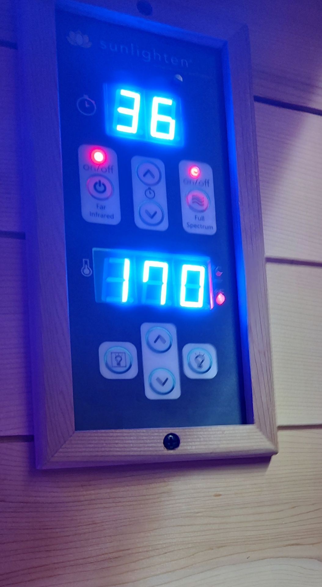 Digital control panel of a sauna with illuminated temperature and timer displays, surrounded by wooden walls.